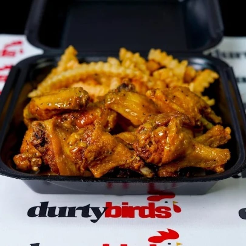 Durty Birds' golden-brown chicken wings and crinkle-cut fries in a black takeout container.