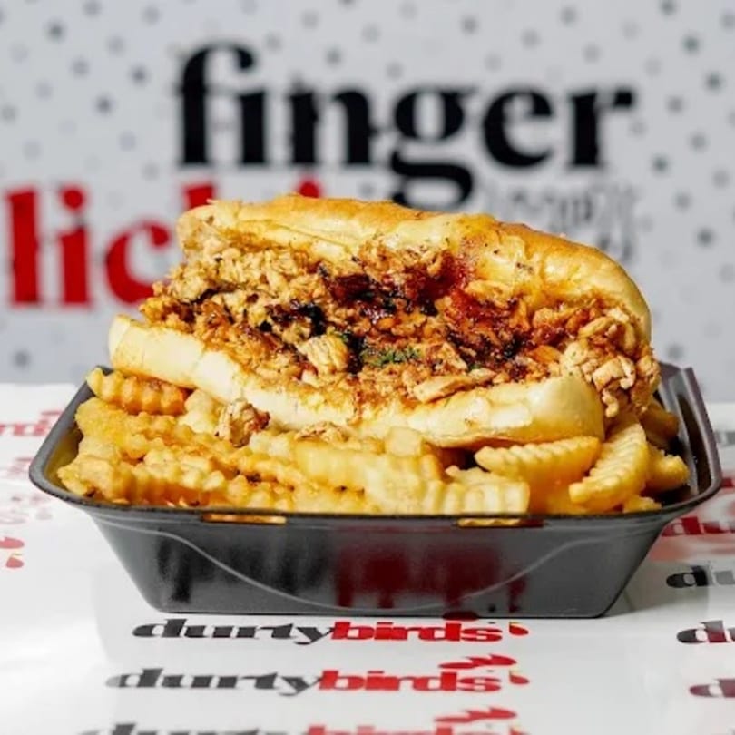 A Dirty Birds chicken sandwich with crinkle-cut fries in a black tray on a branded paper.