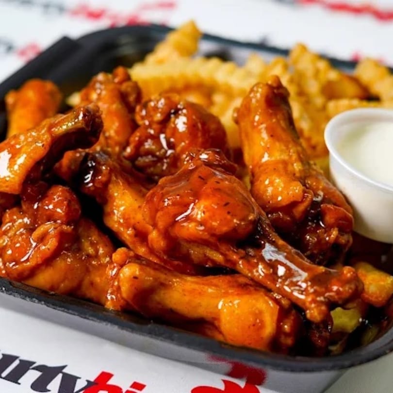 A black tray of saucy chicken wings, crinkle-cut fries, and a side of ranch dressing.